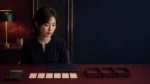 女性在酒紅桌前看計算機、空白卡片與三個空盒，整理節數檯費與扣項